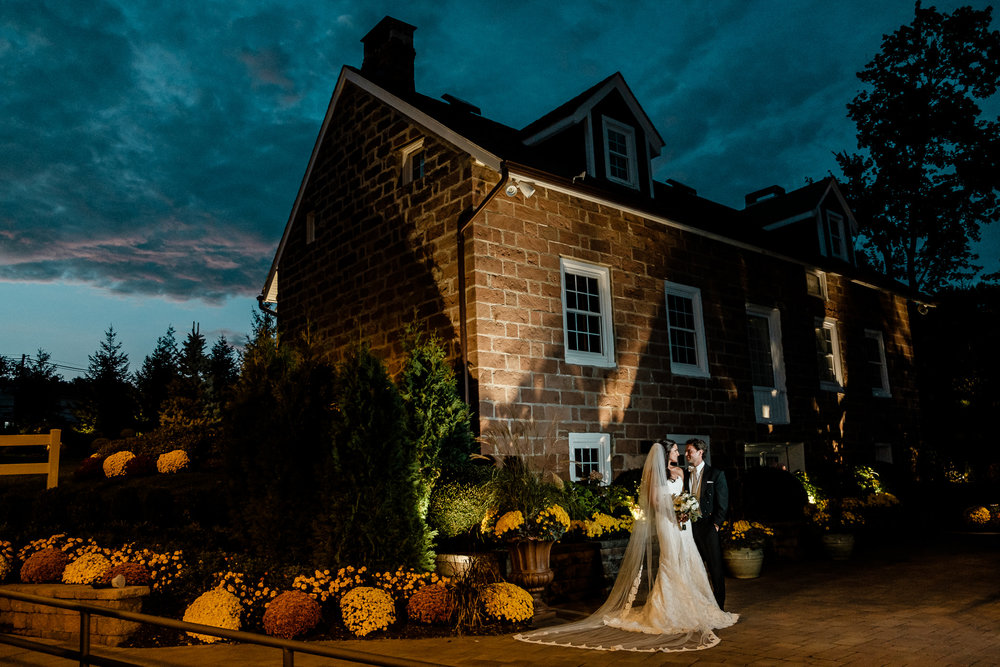 Photograph of Bride and Groom embracing under a blue dark sky at the historic cottage at The Gove with warm orange ambient light and fall decorations