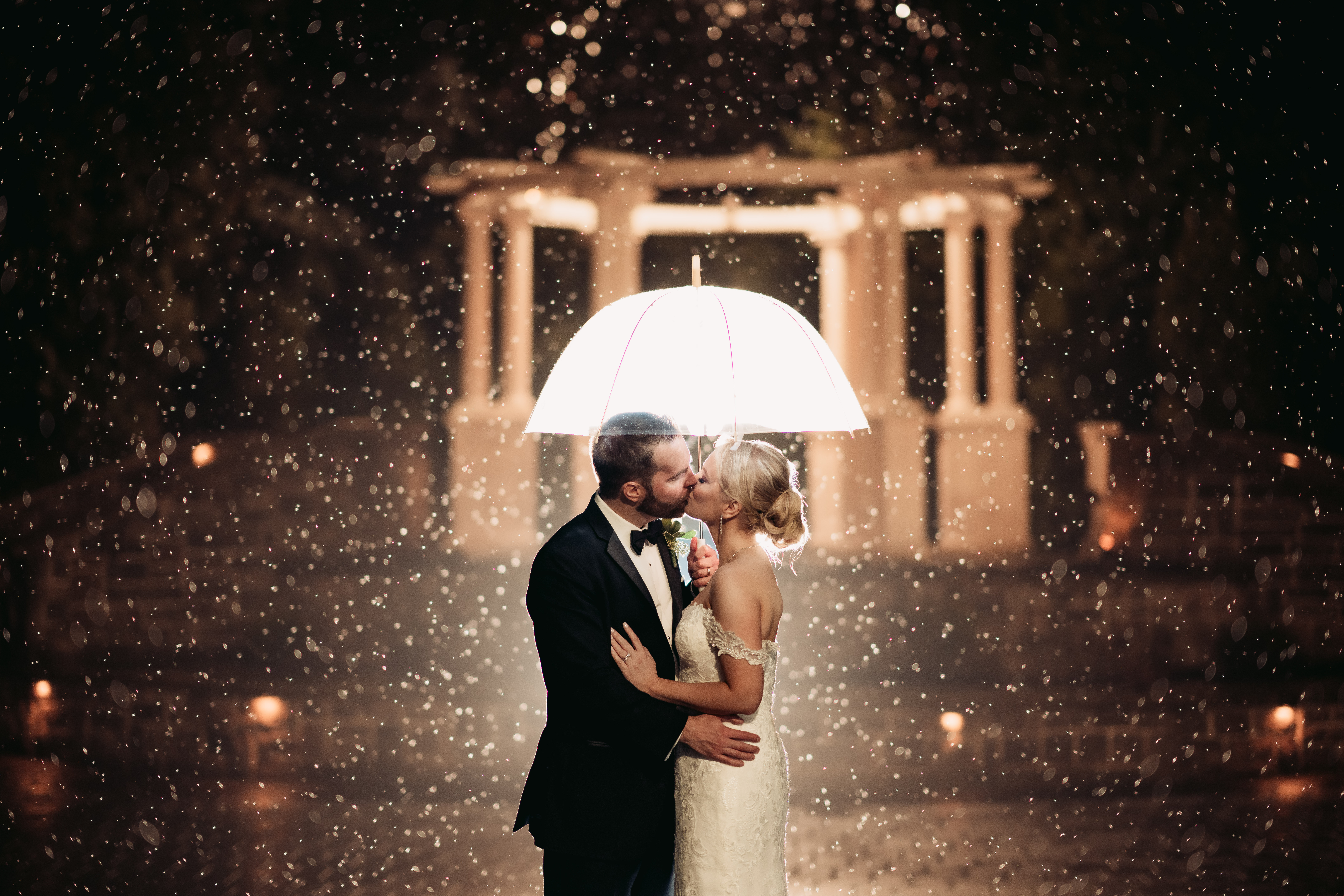 Valley Regency Wedding Photographer, Vally Regency Wedding Venue, New Jersey Weddings, NJ Wedding Photographer, Montclair Weddings, Montclair Wedding Photographer, NJ Winter Wedding, Winter Wedding, bride and groom kissing while holding a clear umbrella as it snows around them while being backlit with a flash 