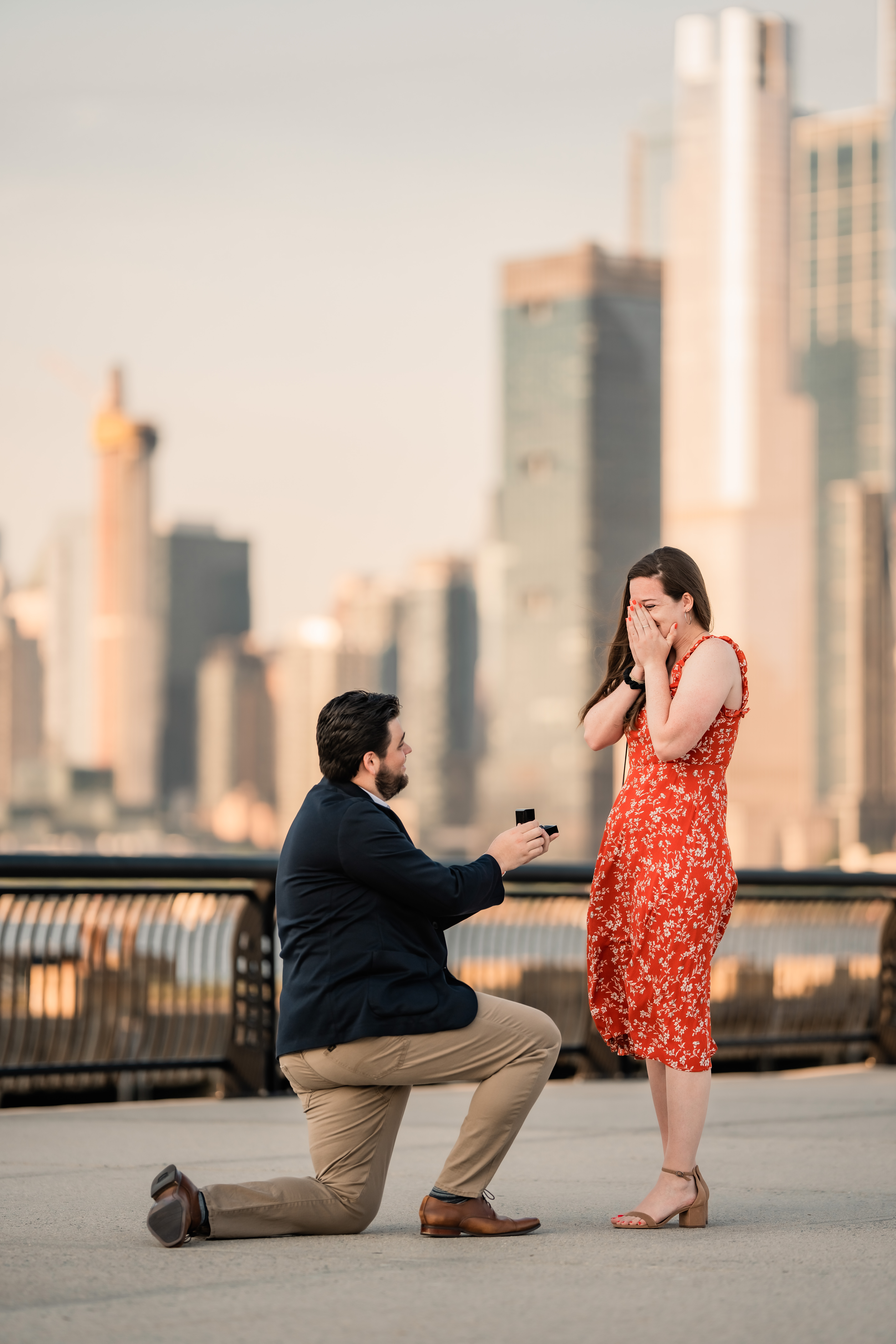 Hoboken New Jersey Proposal, Hoboken Proposal, Hoboken Proposal Photographer, Hoboken Photographer, New Jersey Photographer, NJ Engagement Photographer, NJ Winter Proposal, man kneeling down to propose to his fiancé as she covers her face in happiness with the New York skyline 