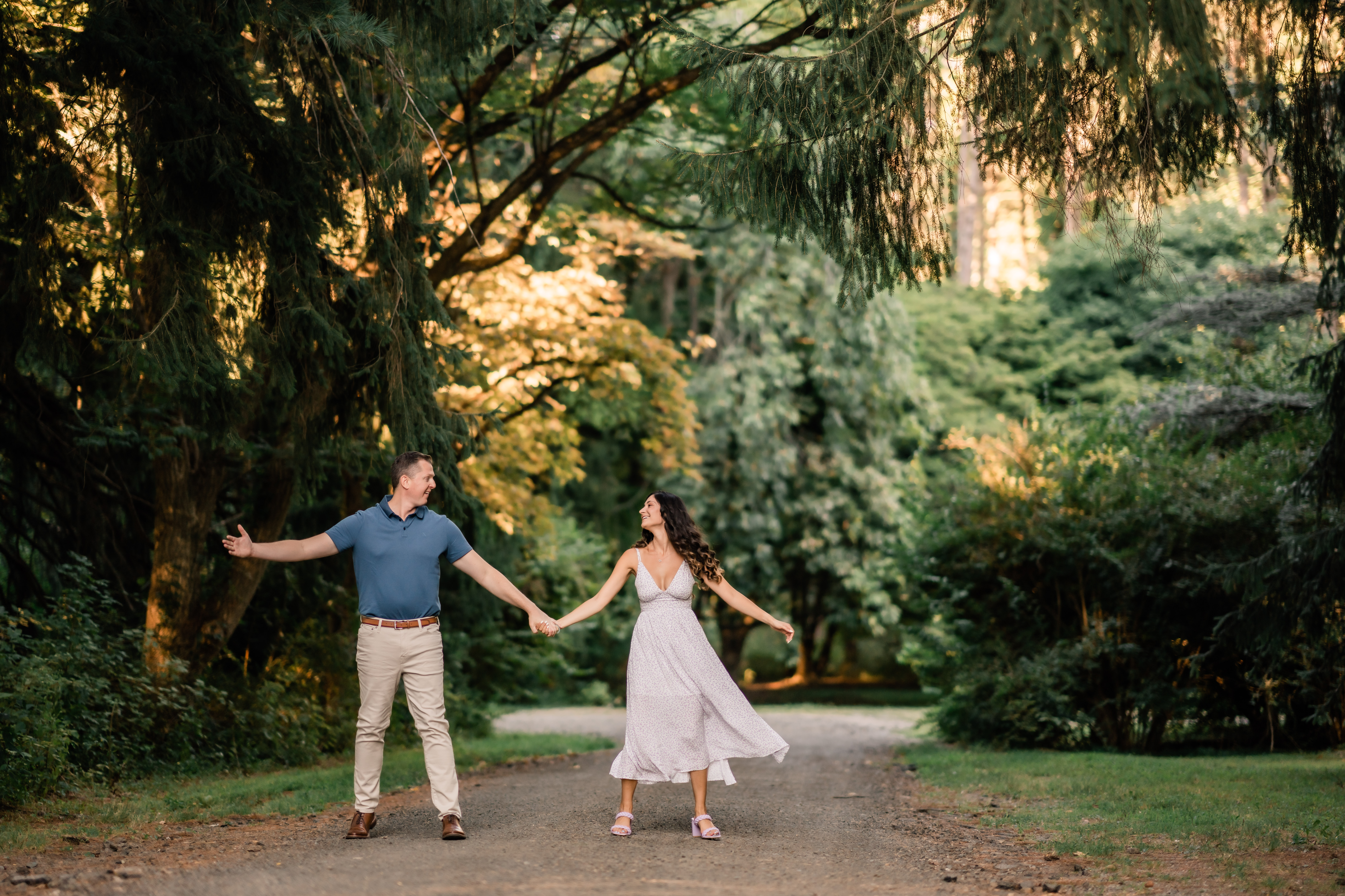 Cross Estate Gardens Engagement, Cross Estate Gardens Engagement Photographer, Bernardsville NJ Photographer, NJ Engagement Photographer, couple smiling at each other holding their arms out dancing while surrounded by green trees and bushes