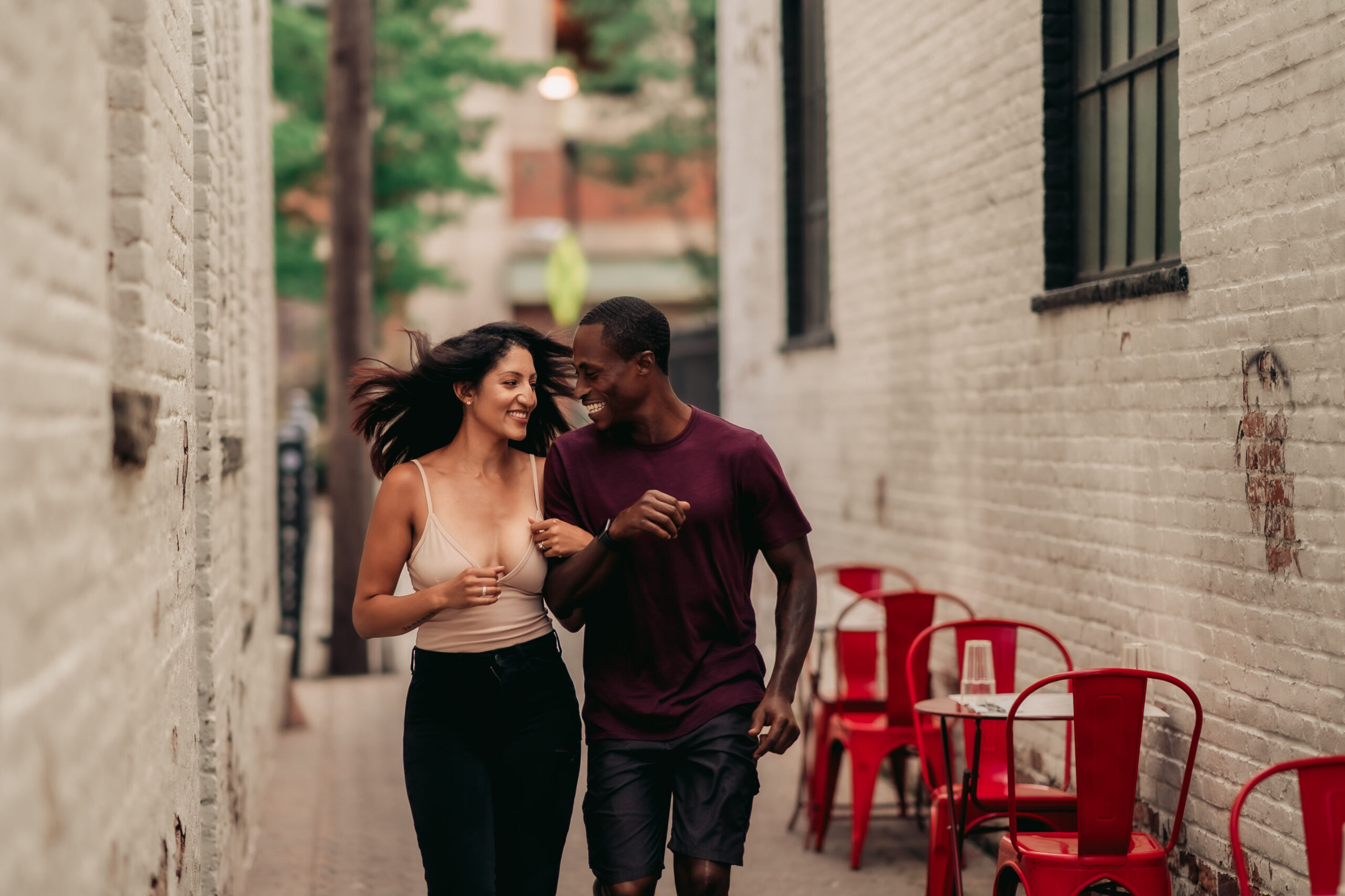 Montclair Engagement, Montclair NJ Engagement Photographer, Montclair Photographer, NJ Engagement Photographer, POC couple running through an alley in Montclair while holding each others arms and smiling and looking at each other
