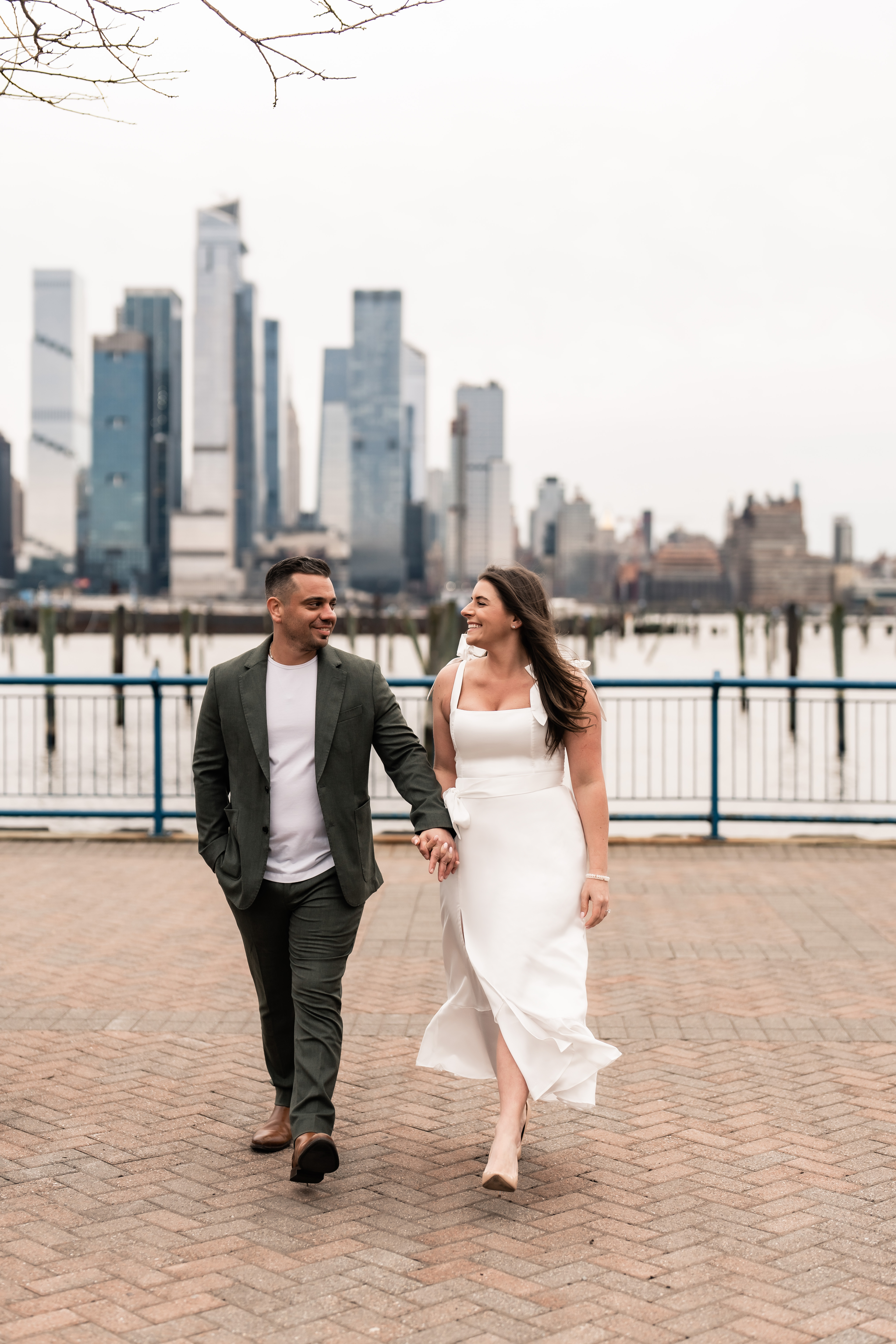 Hoboken New Jersey Wedding Photographer, Hoboken New Jersey Engagement Session, NJ Engagement Session, Hoboken  Wedding Photographer, New Jersey Wedding Venues, NJ Wedding Photographer, Unique Wedding Ideas, Wedding Planning, Save The Date Photos, Engaged couple holding hands and walking towards photographer as they smile and look at each other with New York City in the background 