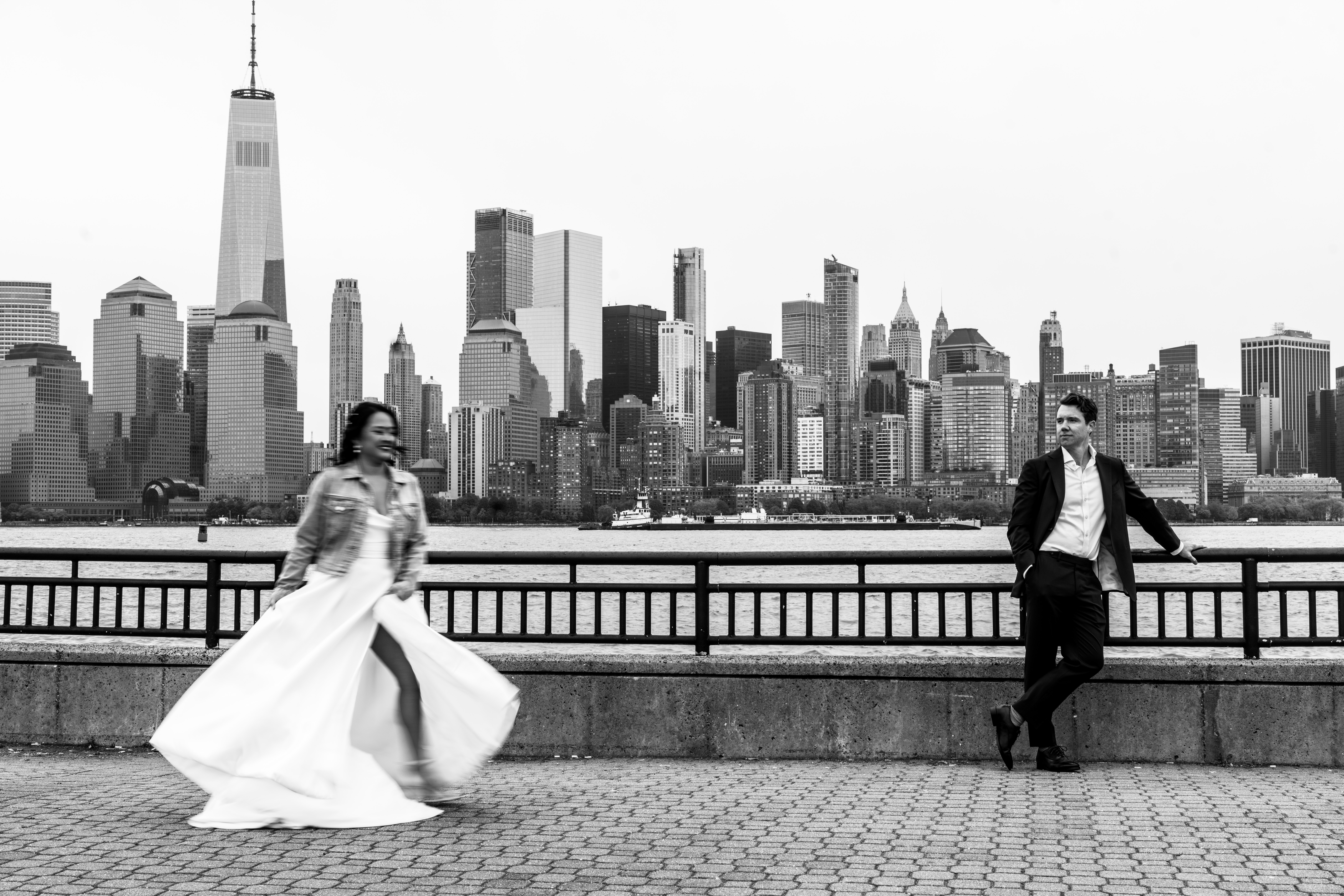 Liberty House Wedding Photographer, Liberty House Wedding Venue, New Jersey Weddings, NJ Wedding Photographer, Jersey City Weddings, Jersey City Wedding Photographer, NJ Summer Wedding, Summer Wedding, groom standing against the railing as his bride twirls out of focus in front of him with the New York City skyline in the background. 