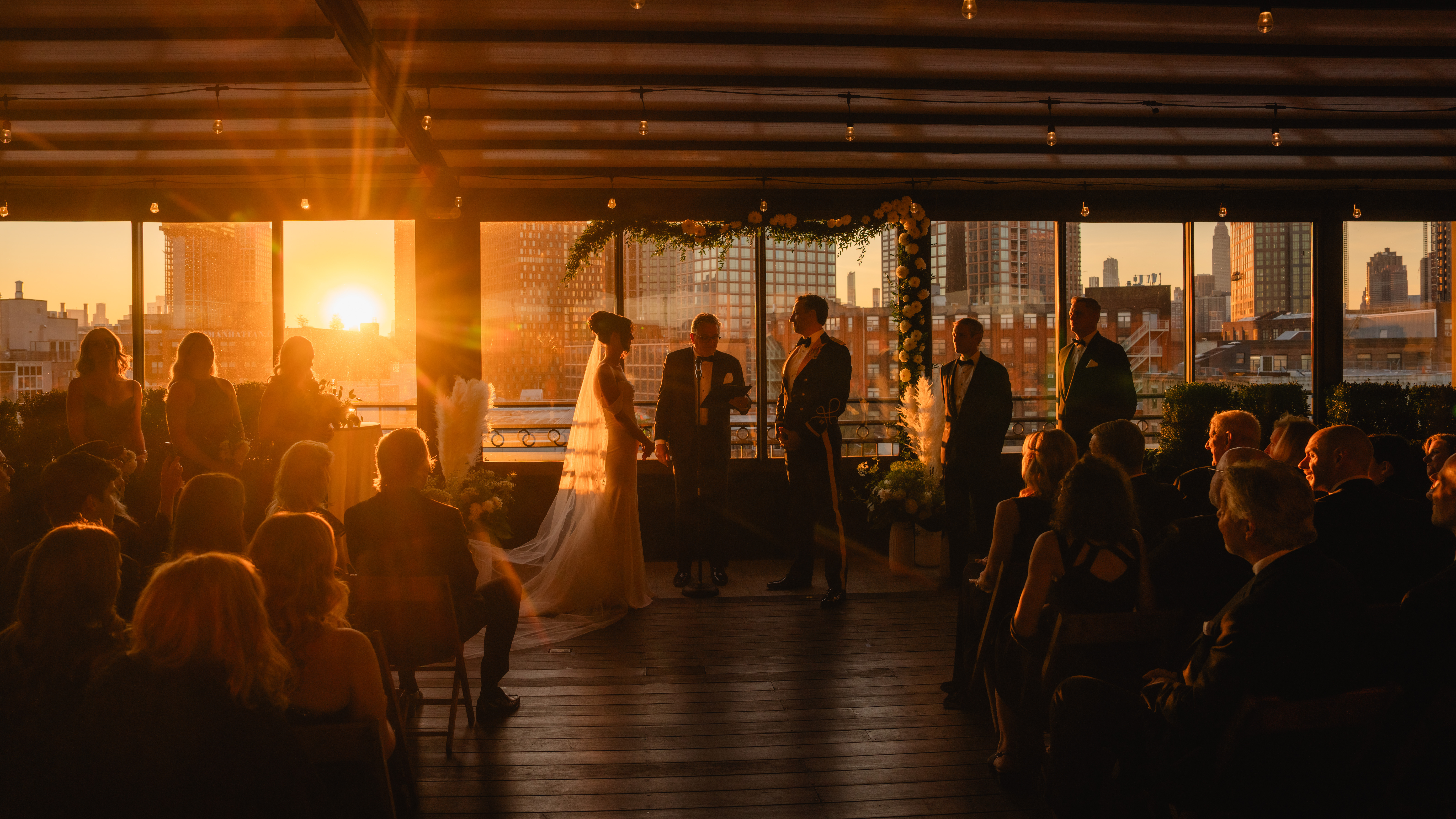 Box House Hotel Wedding, Brooklyn Wedding Photographer, NYC Wedding Photographer, NJ Wedding Photographer, Brooklyn Chic Wedding, Brooklyn Wedding Venue, NYC Wedding Venue, NYC Wedding, Disco Ball Wedding, Wedding Photo Inspiration, Wedding Photo Ideas, Cinematic Wedding Photography, Documentary Wedding Photography, wedding ceremony photo of tall bride and groom wearing Army Officer Blue Mess Uniform crowd silhouetted in golden hour light with NYC skyline in the background.