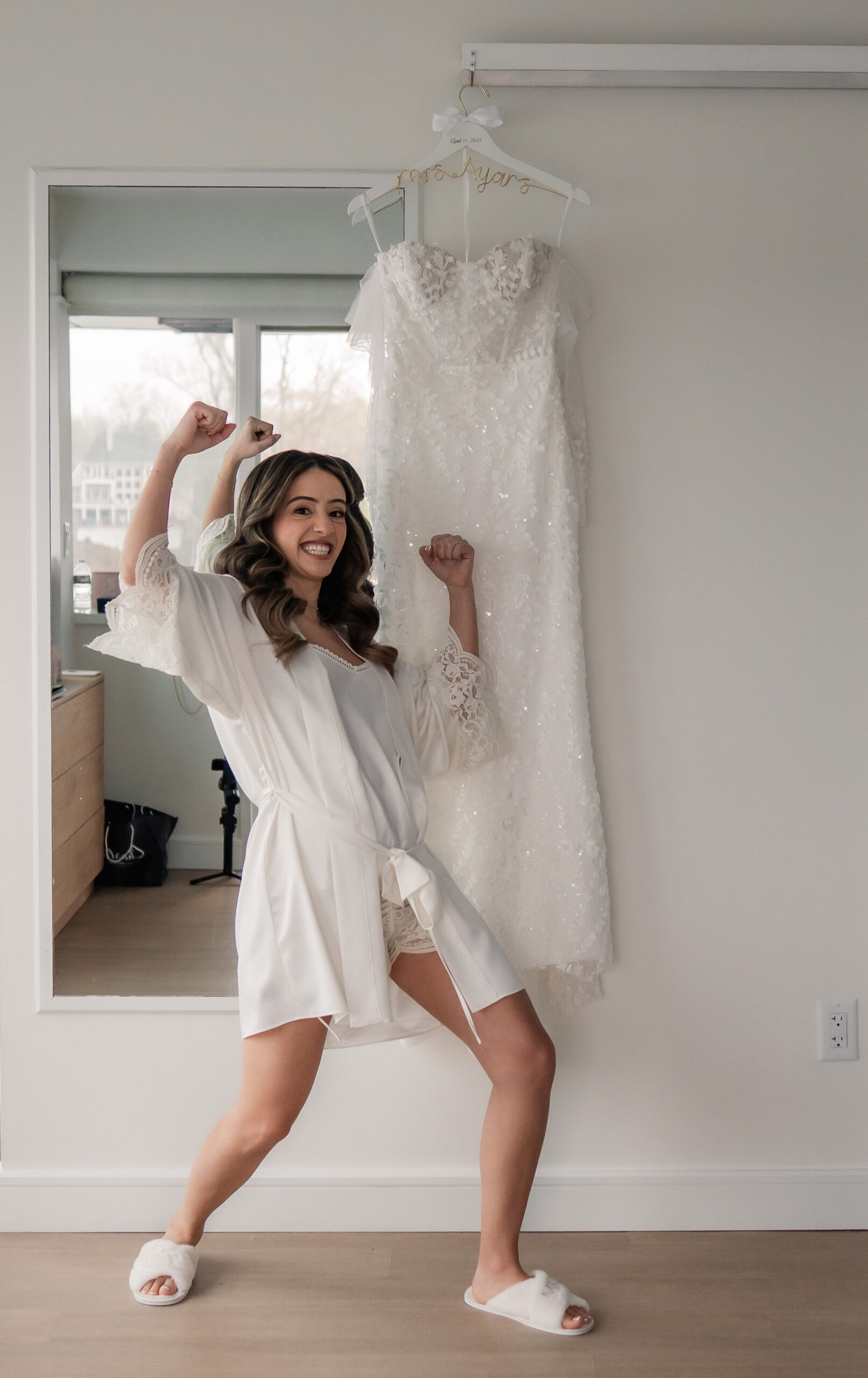 Fun candid bridal getting-ready photo before a Park Loft wedding, with the bride flexing beside her lace wedding dress in a white robe.