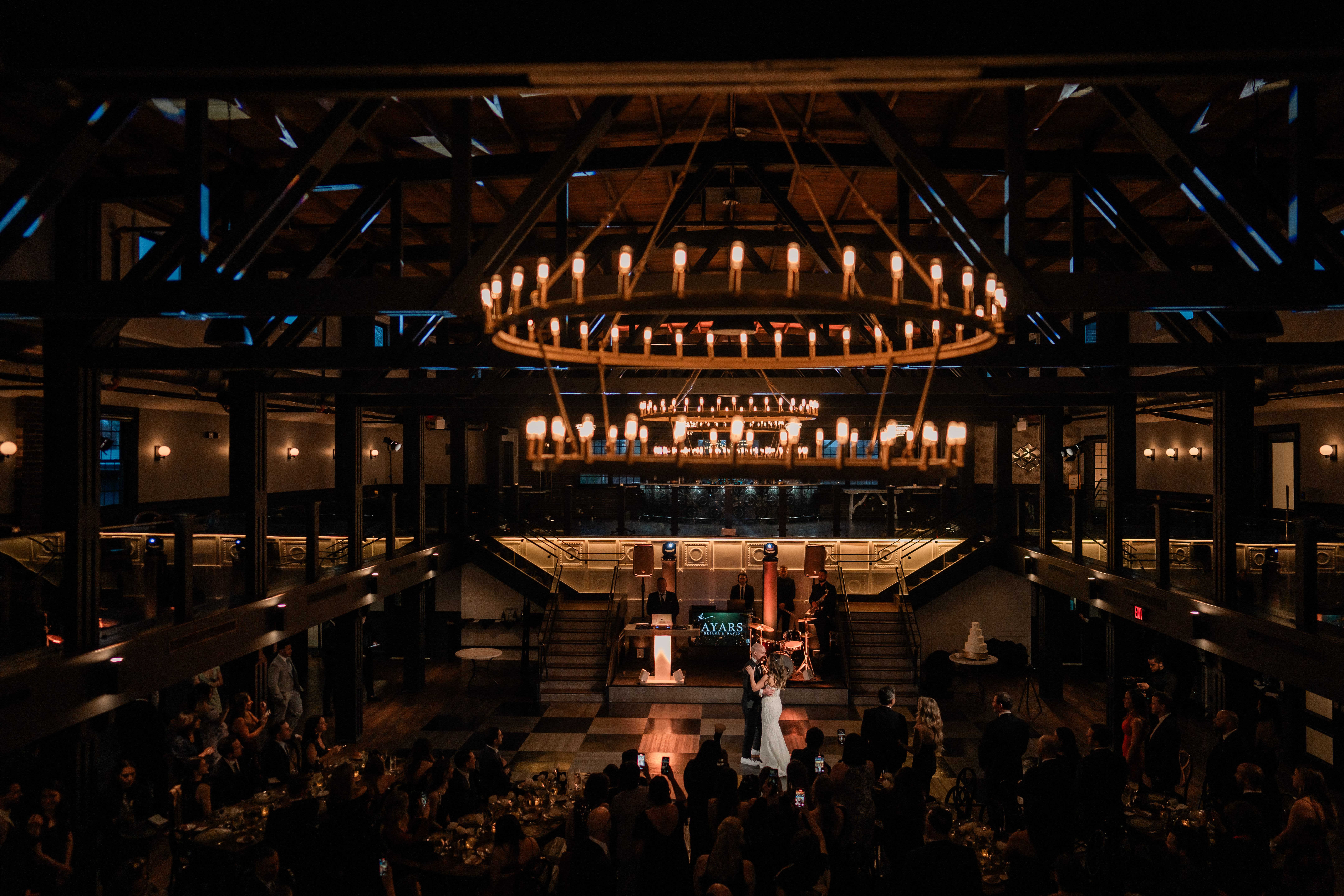 Wide view of a Park Loft wedding reception in Oceanport, NJ, showing the dramatic ballroom, chandeliers, balcony, packed guest tables and dance floor below.
