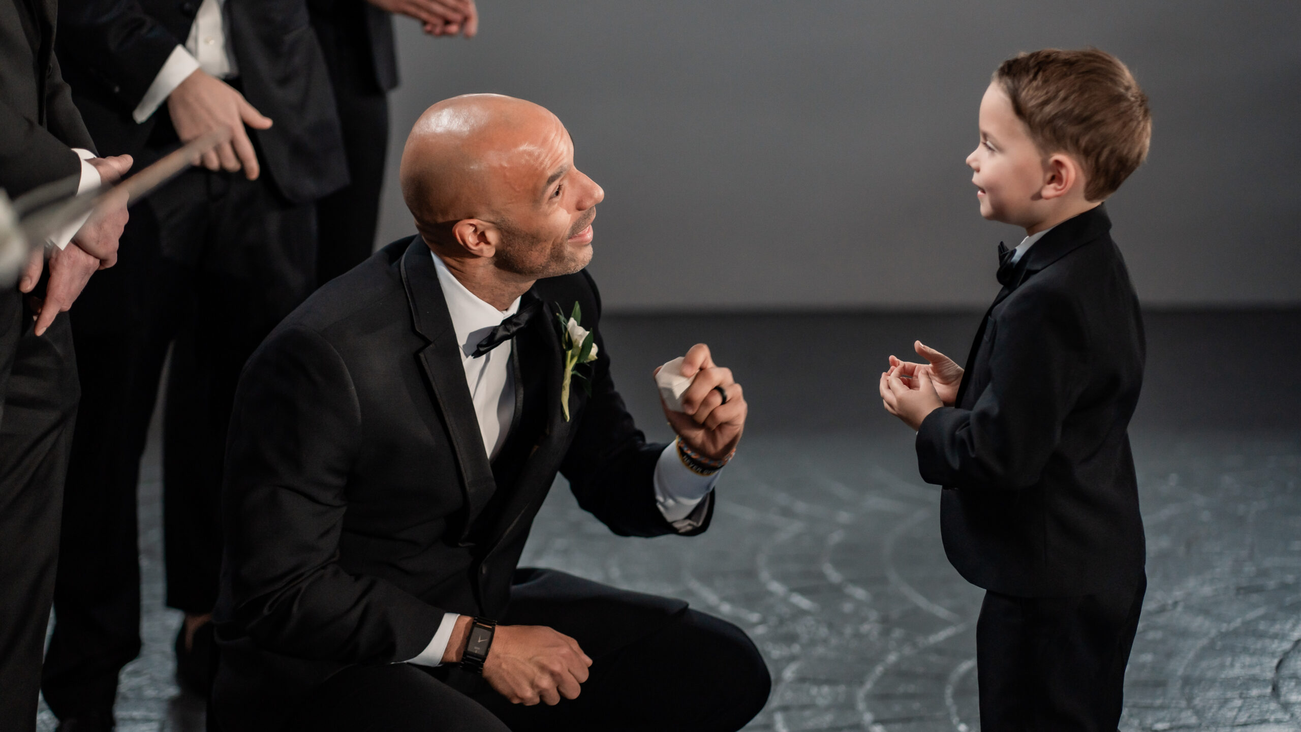 Candid Park Loft wedding photo of the groom kneeling to talk with a young ring bearer before the ceremony in Oceanport, New Jersey.