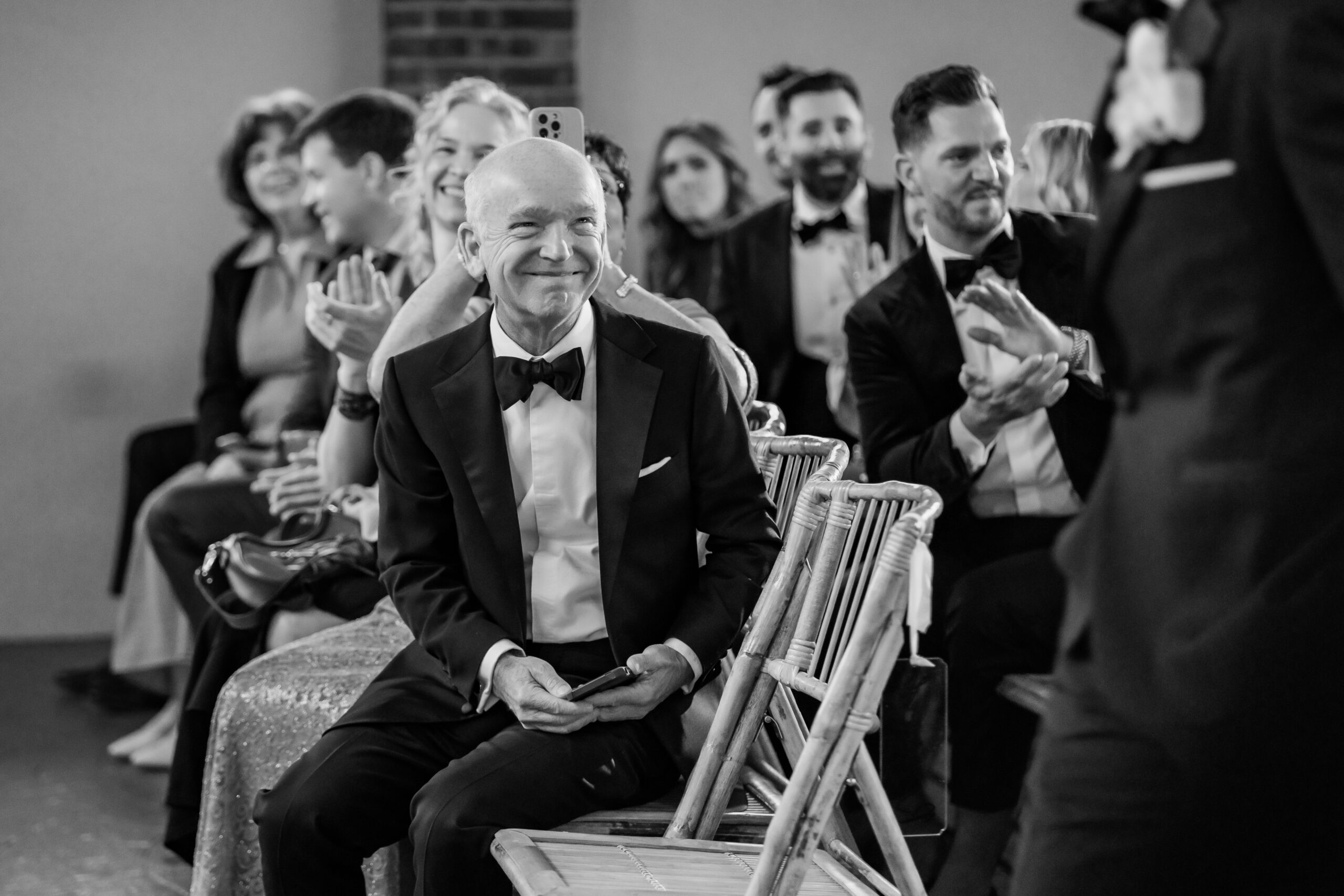 Black-and-white candid New Jersey wedding photo of the groom smiling from his seat during the Park Loft ceremony.