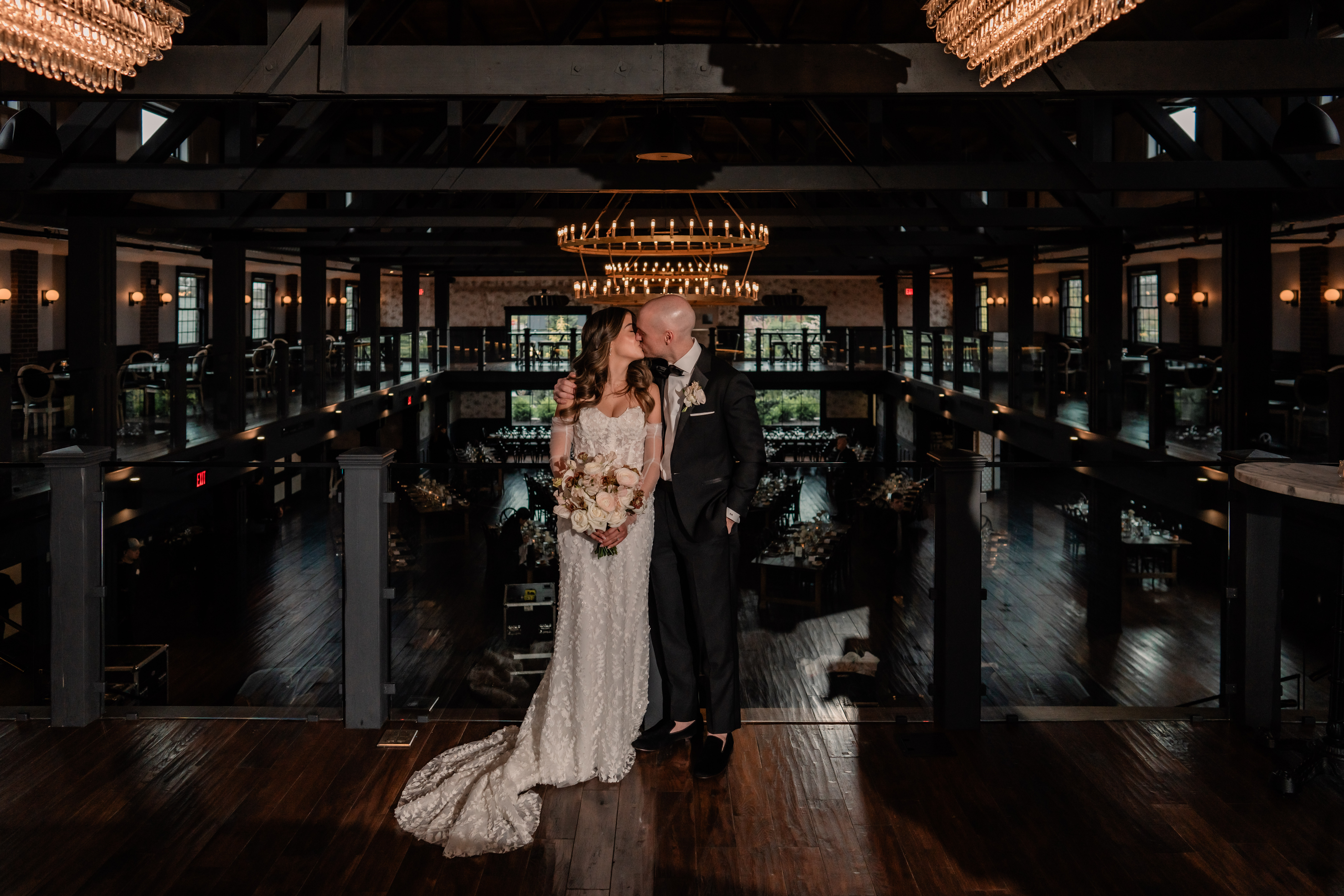 Elegant Park Loft wedding portrait of the bride and groom on the balcony above the ballroom, surrounded by dark wood, chandeliers and modern architecture.