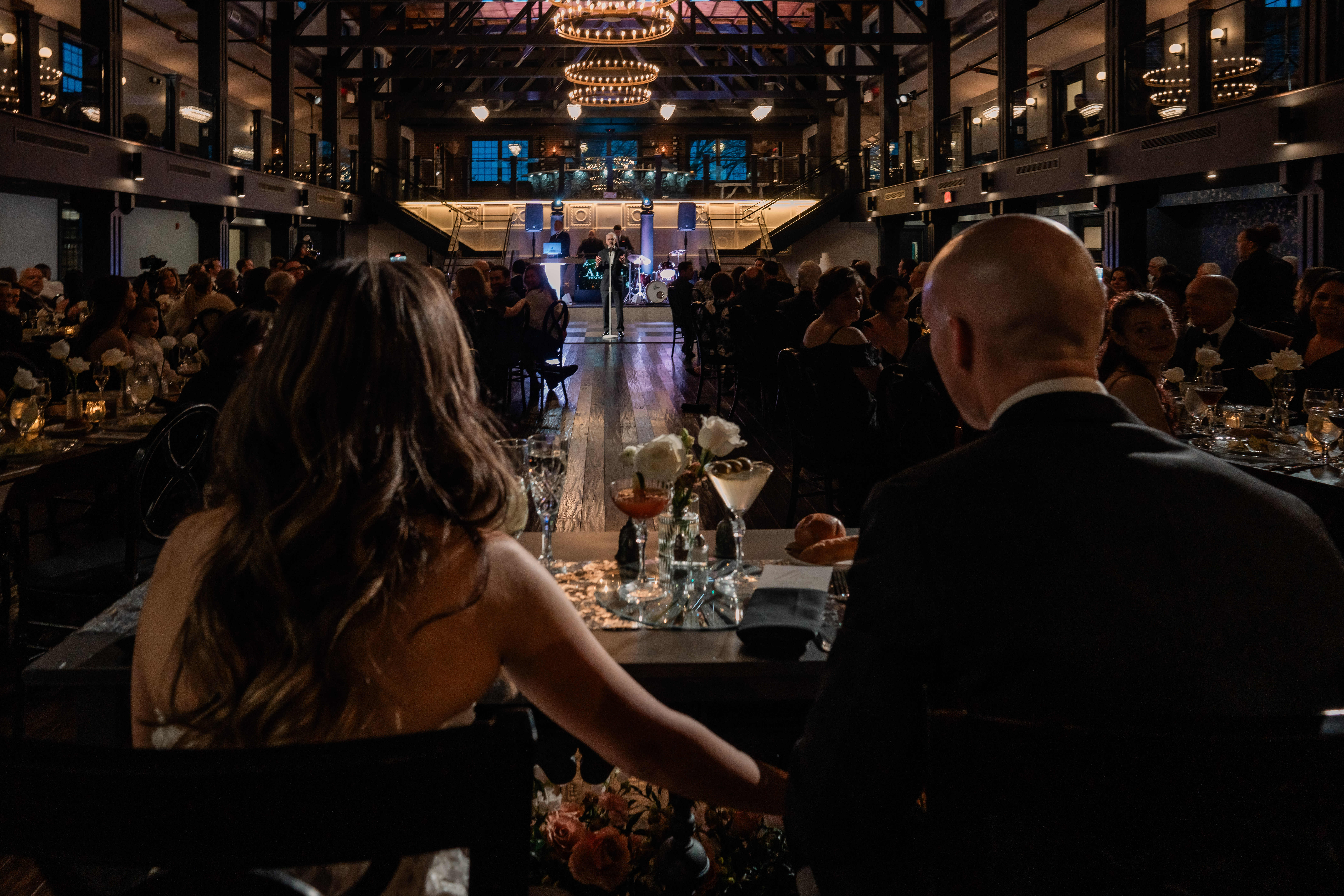 Wide Park Loft wedding reception photo from behind the newlyweds at their sweetheart table, overlooking the dramatic ballroom and dance floor.
