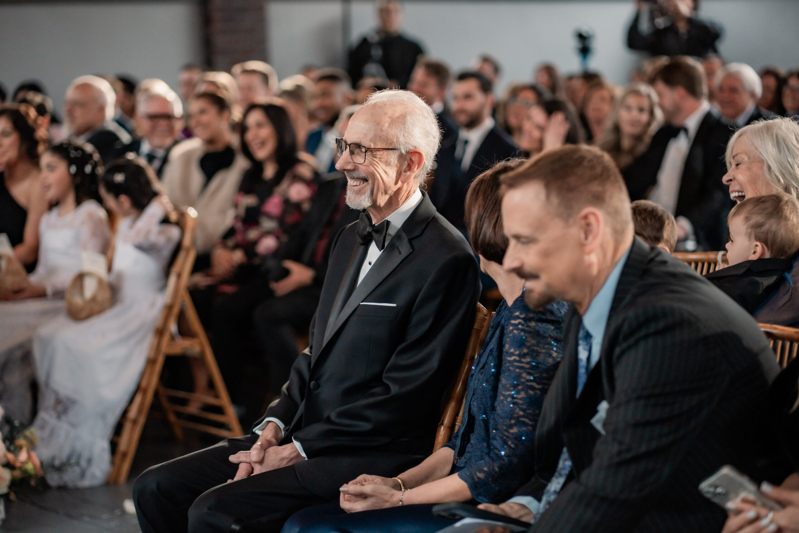 Candid father of the bride reaction during a Park Loft wedding ceremony in Oceanport, NJ, with family and friends smiling from their seats.