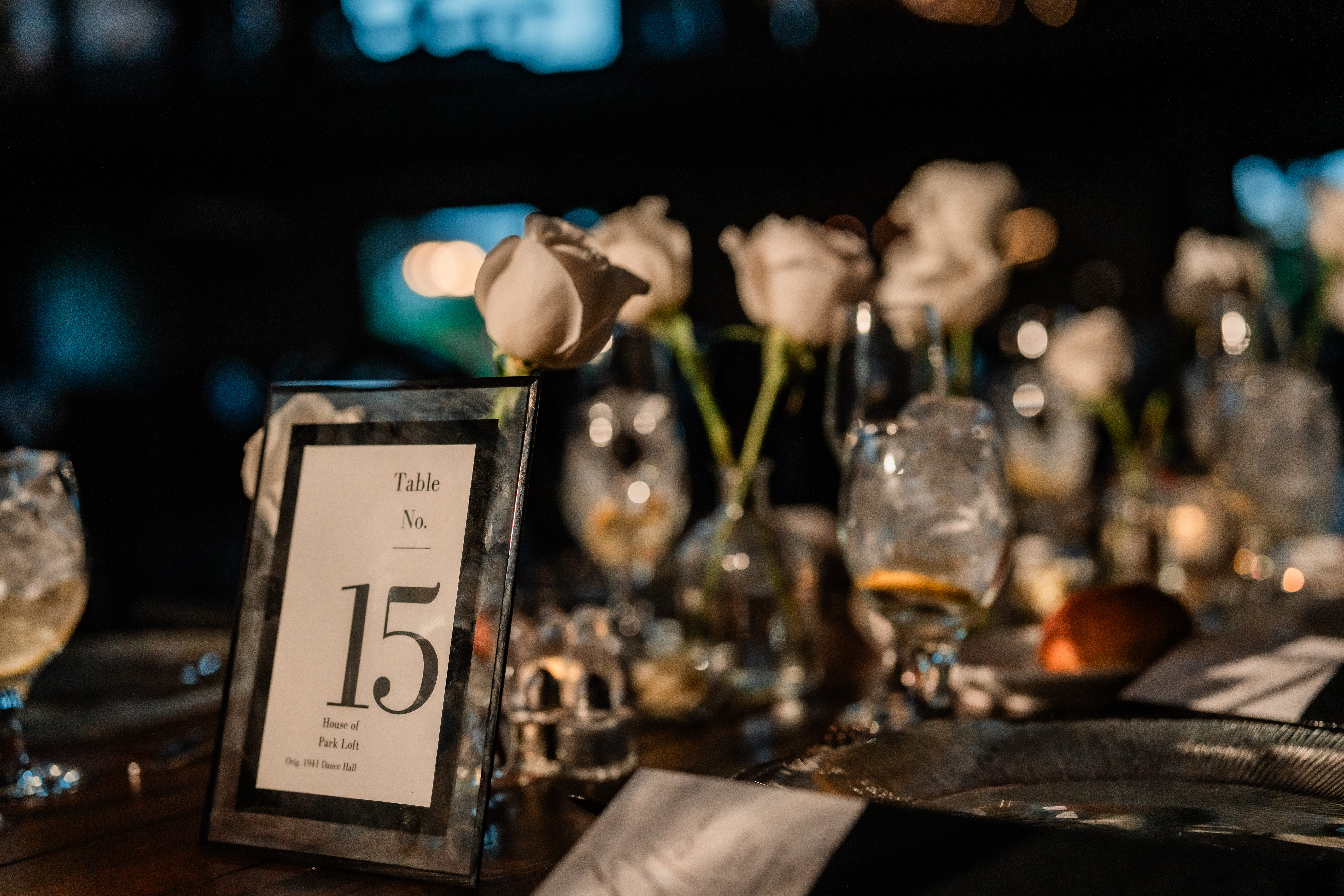 Park Loft wedding reception details in Oceanport, NJ, featuring elegant table numbers, white rose centerpieces and dark modern place settings.