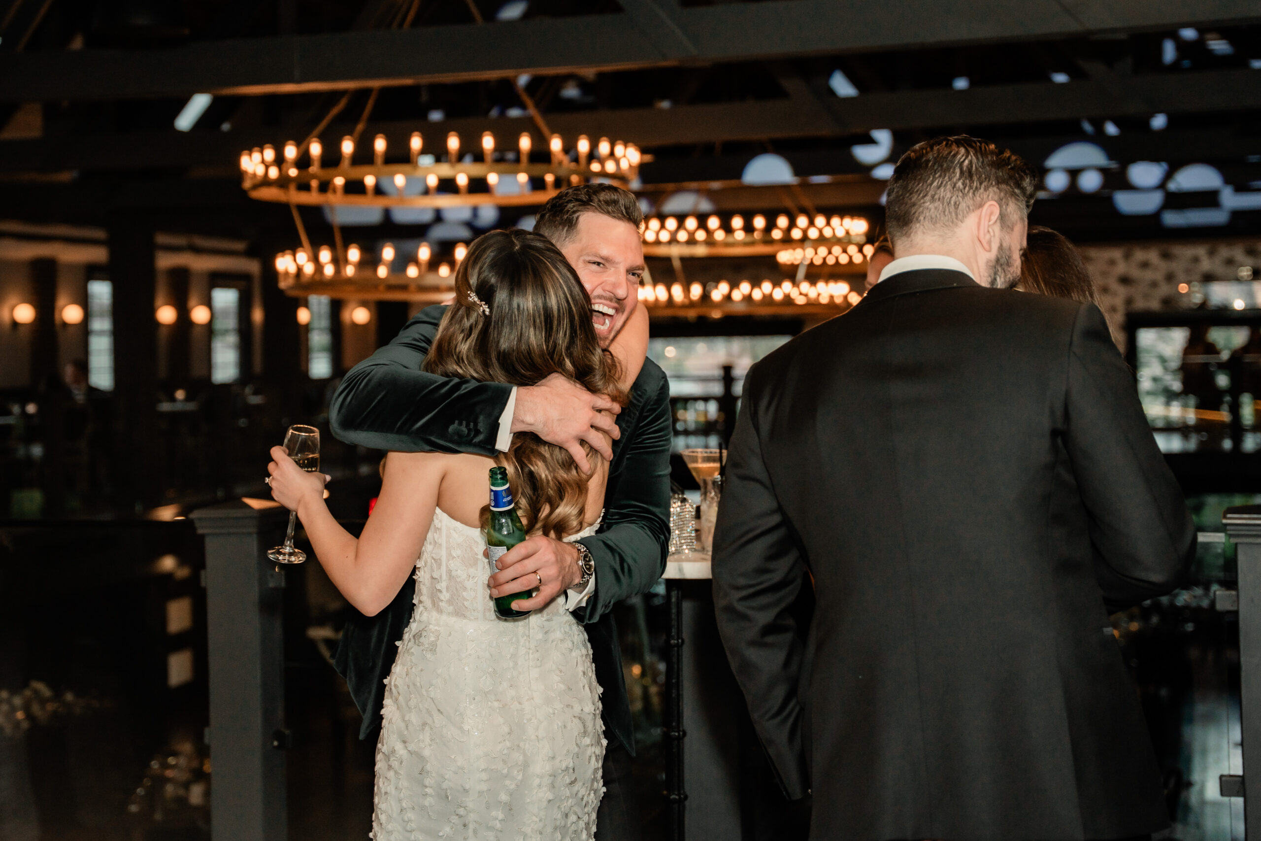 Candid Park Loft wedding photo of the bride hugging a guest during cocktail hour beneath the venue’s dramatic chandeliers.