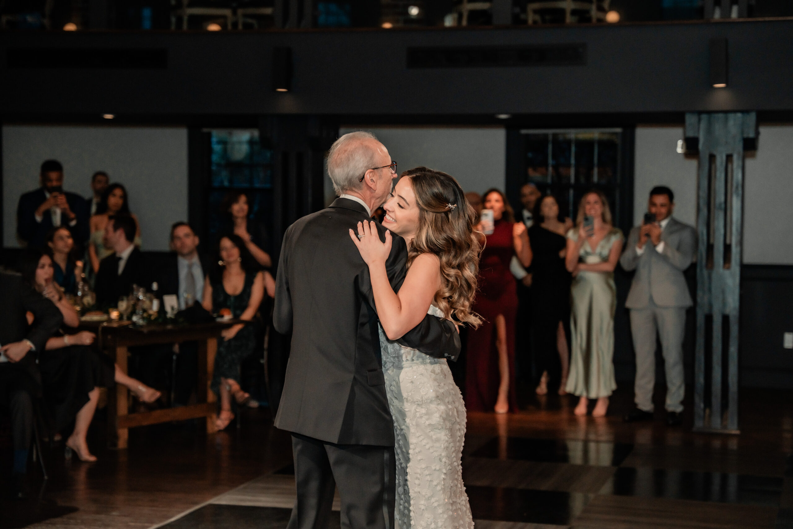 Emotional Park Loft wedding reception photo of the bride dancing with her father while family and guests watch from the ballroom.