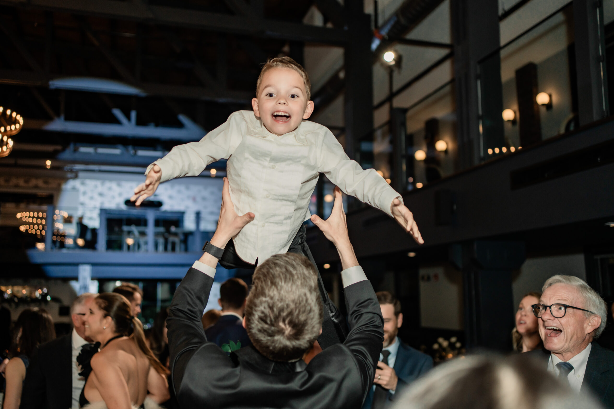 Fun Park Loft wedding reception photo in Oceanport, NJ, with a smiling baby lifted into the air above the crowded dance floor.
