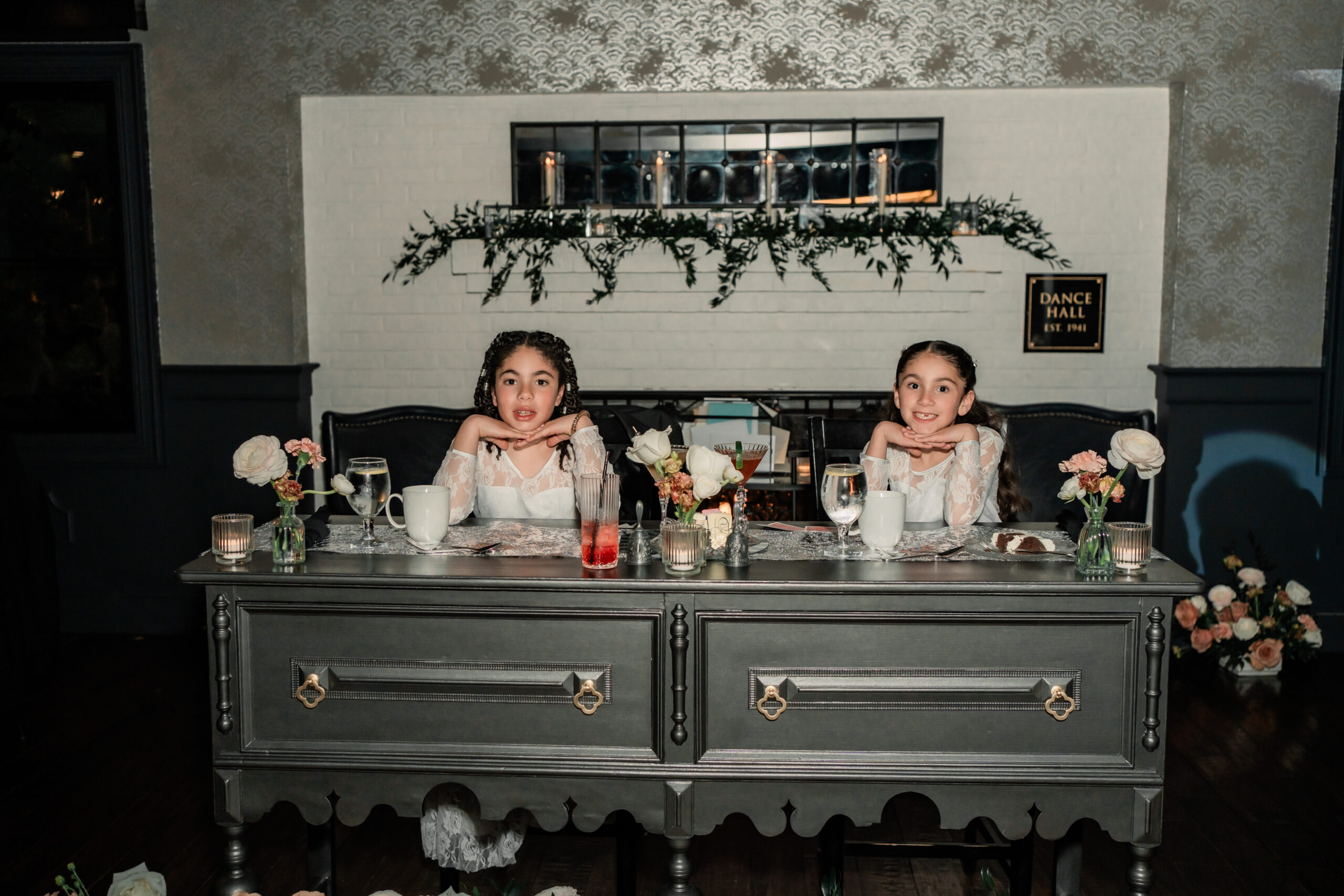 Playful candid Park Loft wedding photo of two flower girls seated at the sweetheart table during the reception in Oceanport, NJ.