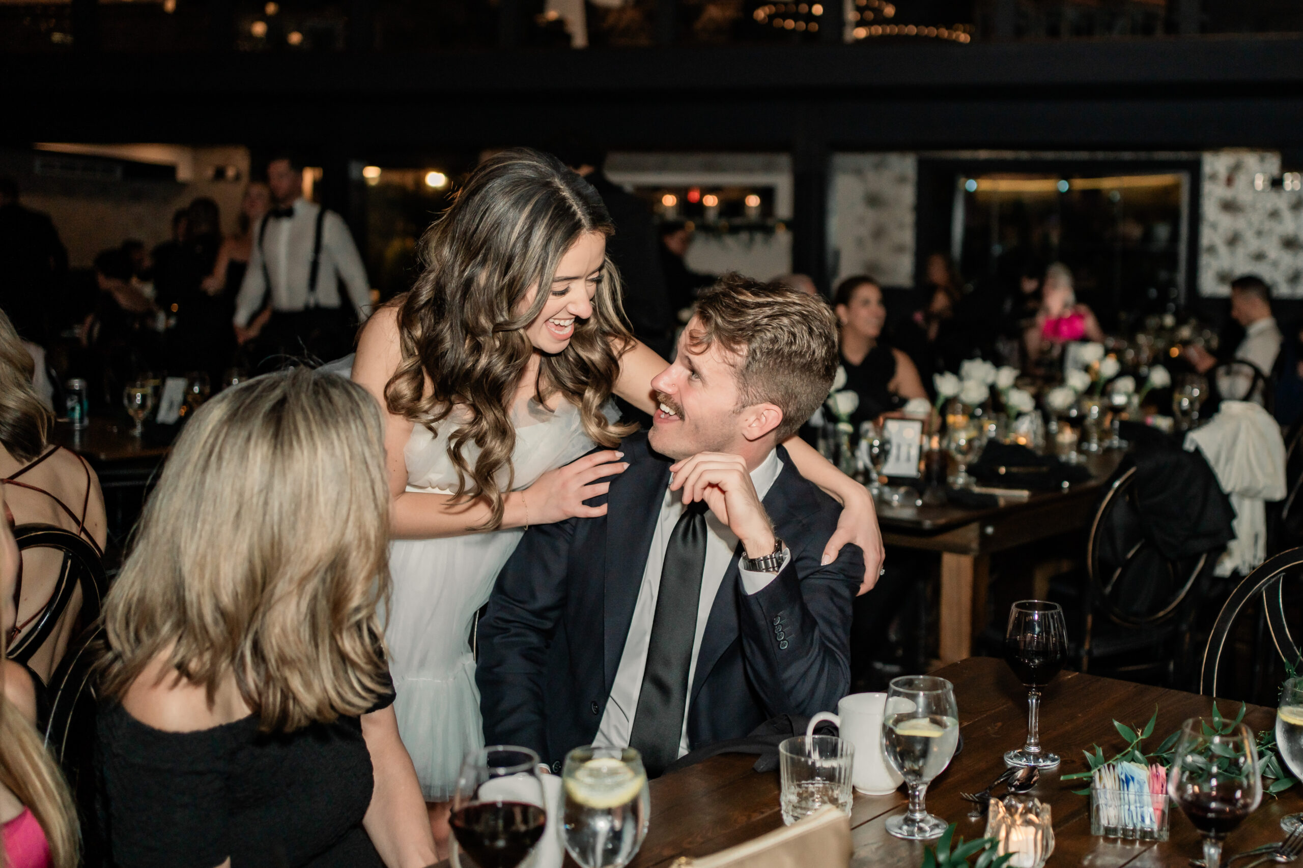 Candid Park Loft wedding reception photo of the bride leaning in to laugh with a seated guest during the party.