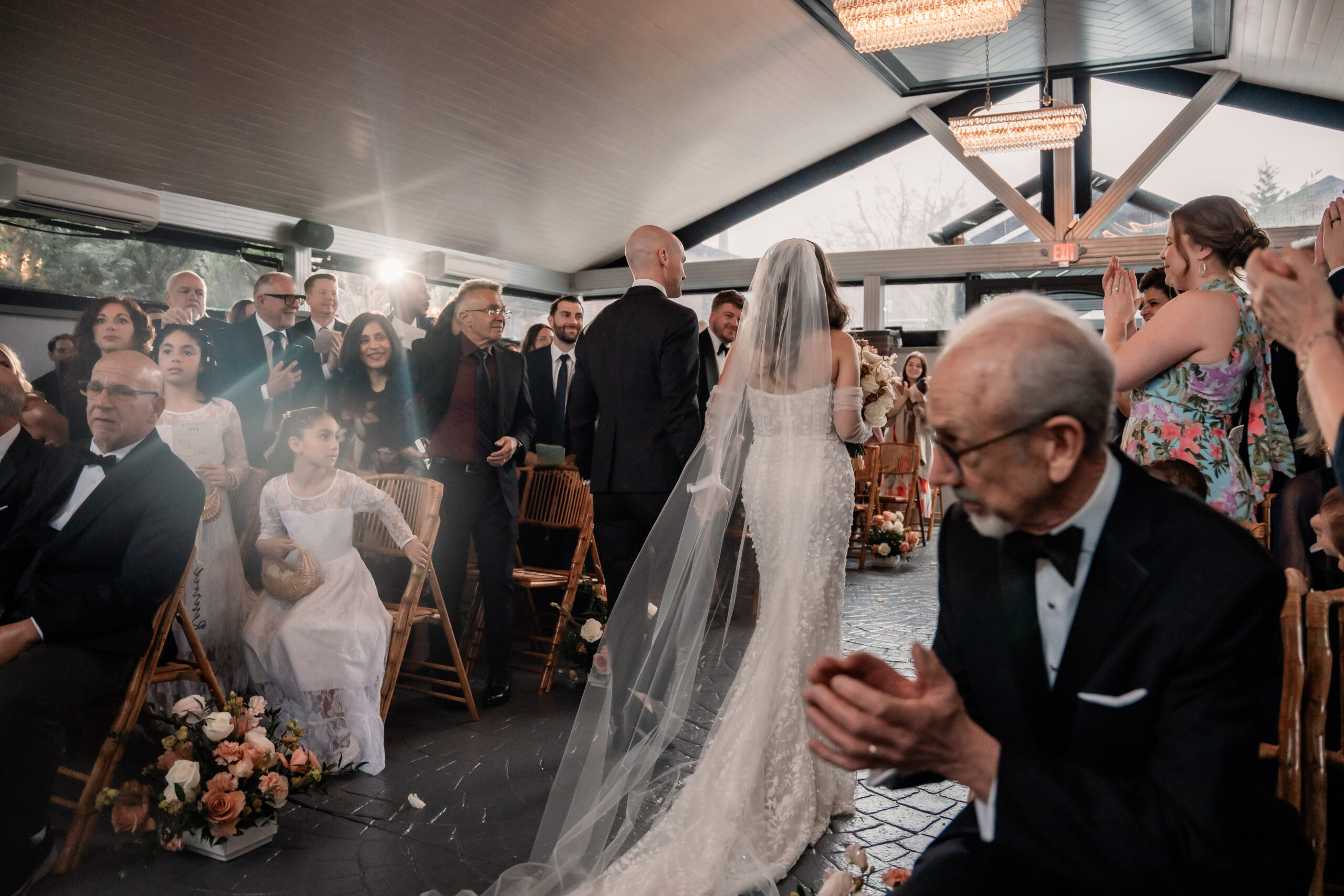 Candid New Jersey wedding photography at Park Loft, capturing the bride and groom from behind walking up the aisle together as guests applaud around them.